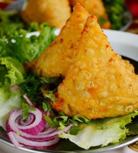 Close-up of crispy samosas served with fresh lettuce and onion rings.